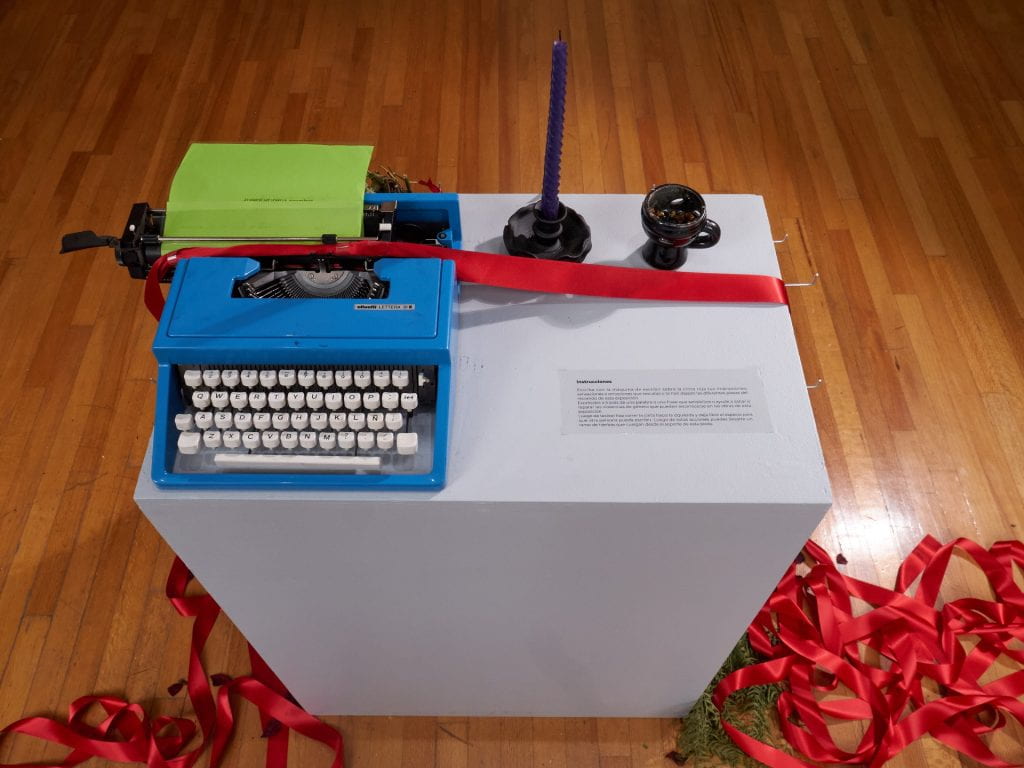 Artwork: Blue typewriter with green sheet of paper loaded. Red ribbon spooling off the dais. 