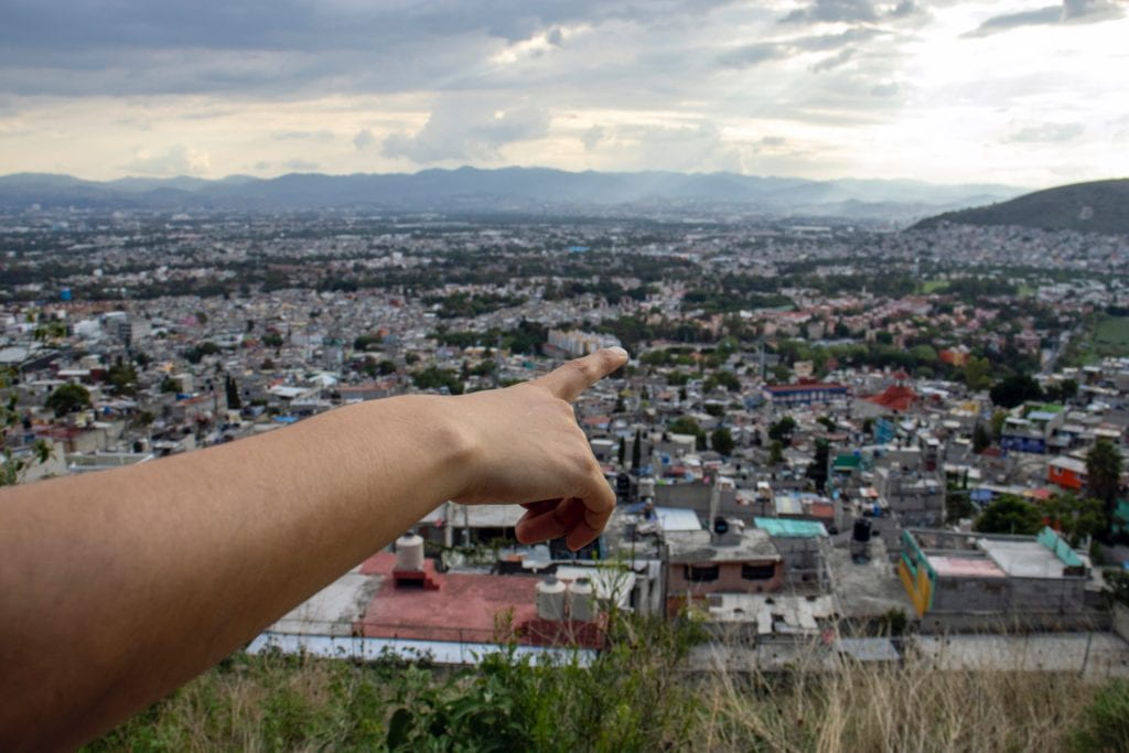 Artwork: finger and forearm in foreground pointing at the city from an elevated vantage point.