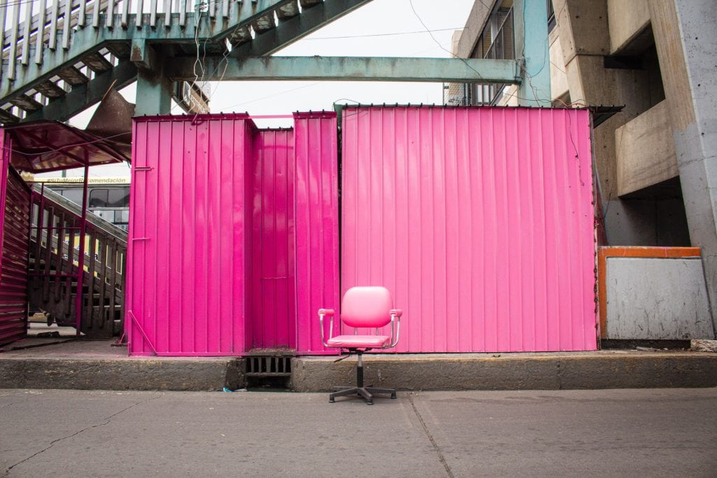 Pink office chair in front of painted pink corrugated metal wall with industrial background.