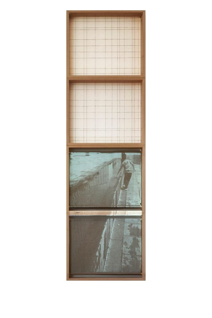 Artwork in four vertical wooden frames. Colour photograph in light box in lower frame showing the back of a caucasian person with long hair and a baseball cap. Black vest top. 