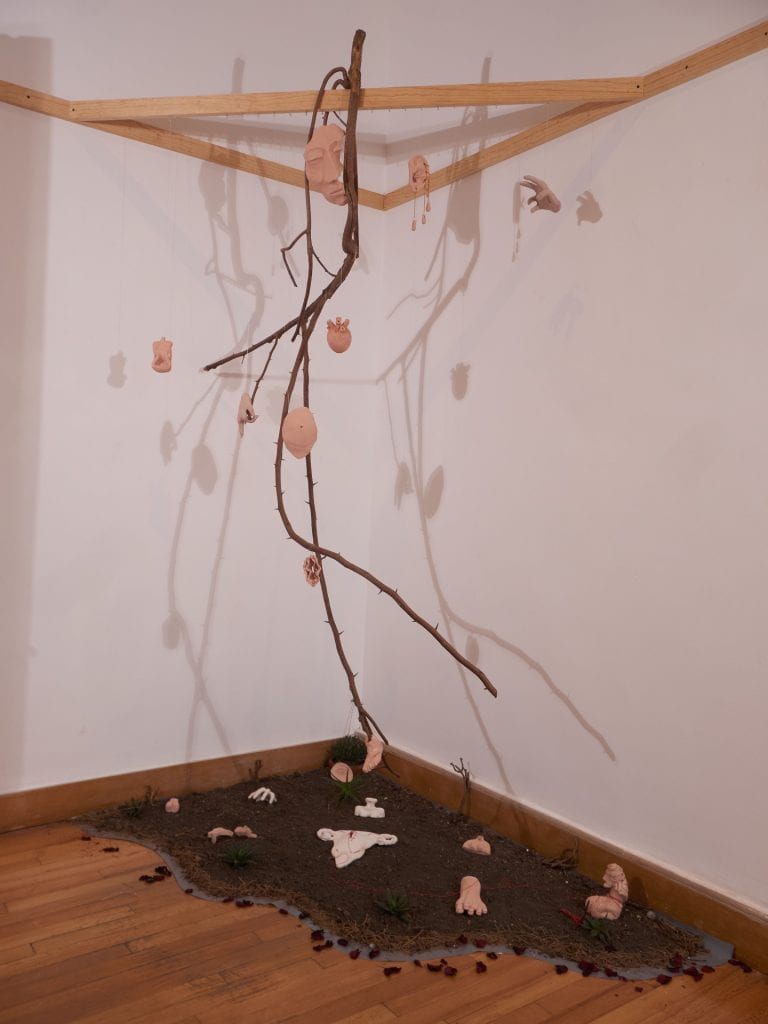 Artwork: branch hanging from corner wooden struts. Shadows on wall of suspended body parts. 