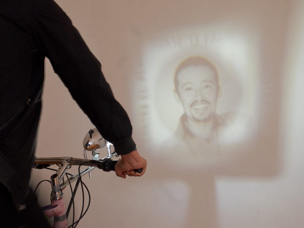 Artwork: person riding a bike and projecting an image of a man.